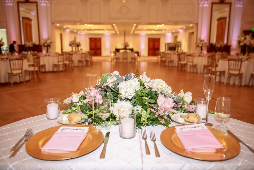 Bride and groom's sweetheart table with gold charger, floral arragement, pink napkins and pintuck tablecloth.