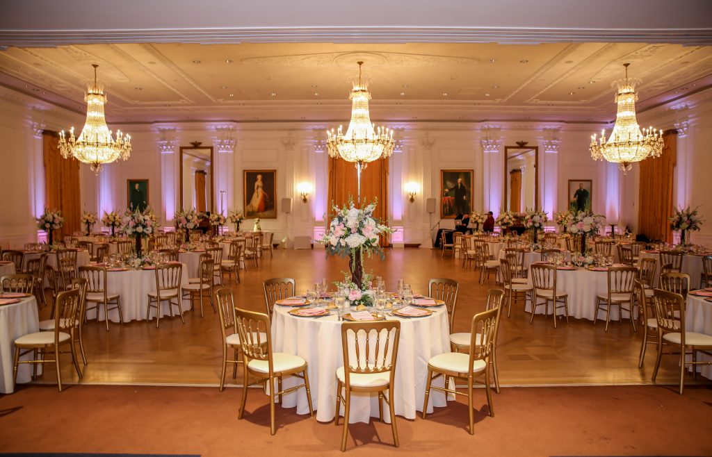 Wedding Reception in the Nixon Library Ballroom with crystal chandeliers and pink uplighting. 